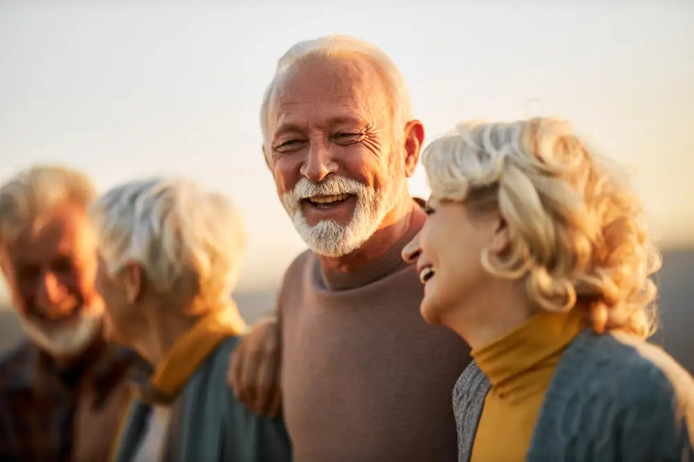 2 elderly couples smiling and hugging each other outside of their home at Amavida In Fort Myers, FL.