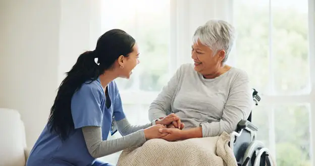 senior woman in her wheelchair with her caregiver kneeling down in front of her