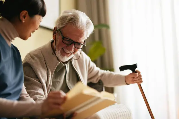 a caregiver and a senior man with a cane looking at a photo album together