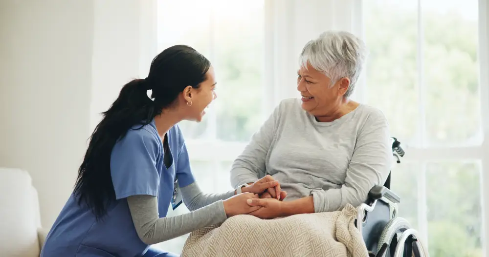 a caregiver comfortingly holding the hands of her senior patient